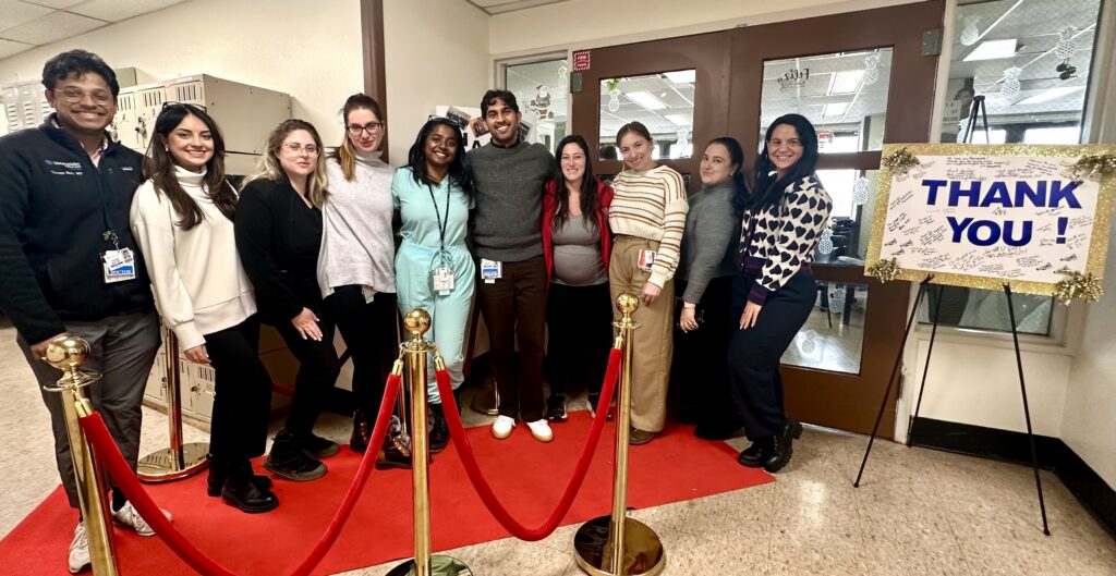 Psychiatry residents pose together on red carpet next to big Thank You sign